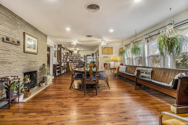 dining area featuring ceiling fan, a large fireplace, and hardwood / wood-style flooring