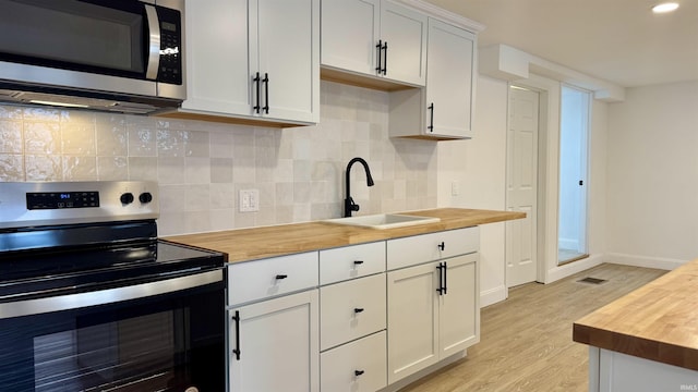 kitchen with appliances with stainless steel finishes, butcher block countertops, white cabinetry, and sink