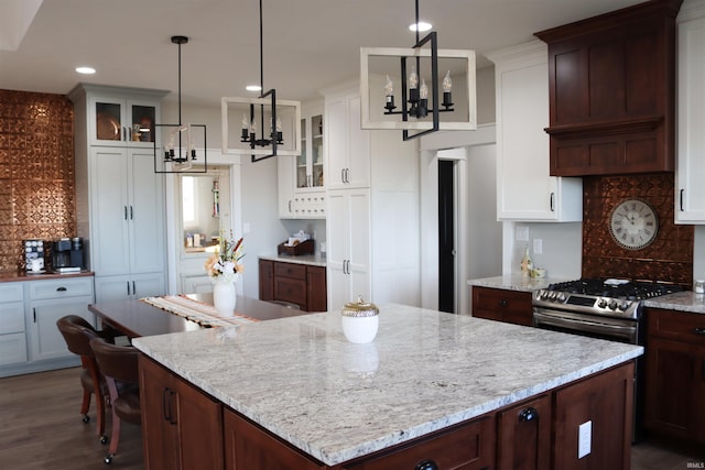 kitchen with white cabinets, tasteful backsplash, stainless steel gas range oven, and a chandelier