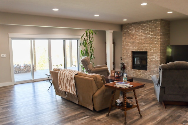 living room featuring dark hardwood / wood-style flooring, ornate columns, and a brick fireplace