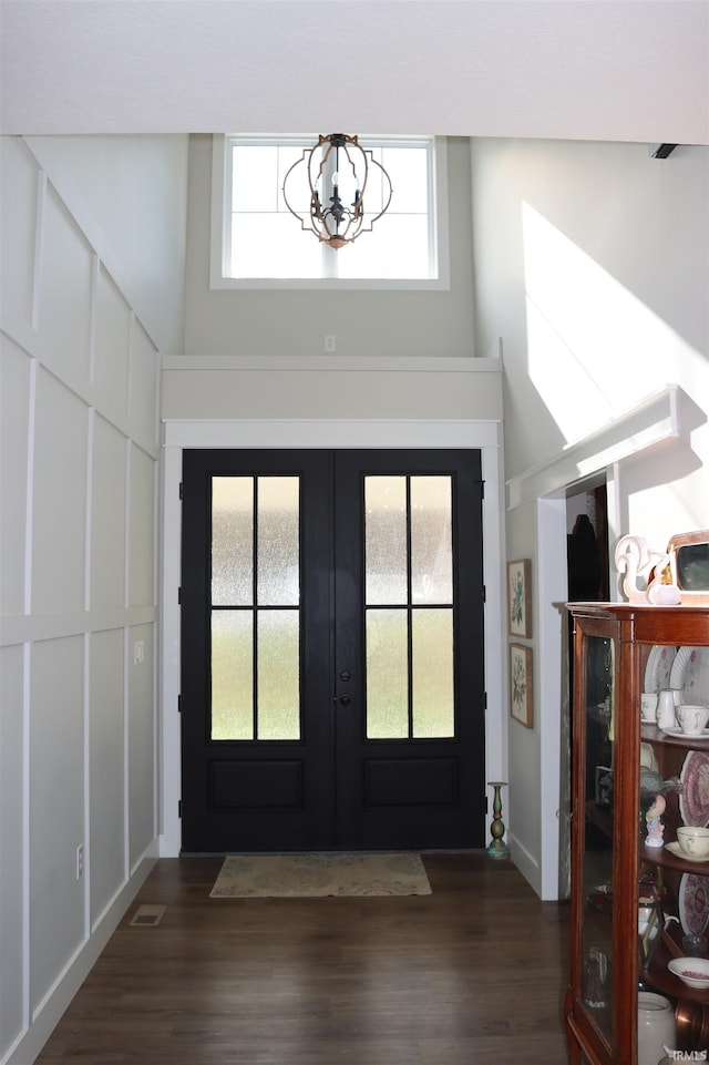 entryway with french doors, a towering ceiling, dark hardwood / wood-style floors, and an inviting chandelier