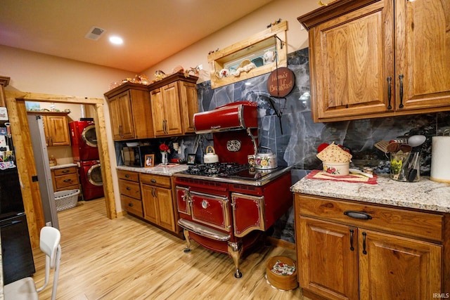 kitchen featuring stainless steel gas stovetop, light stone counters, light wood-type flooring, and backsplash