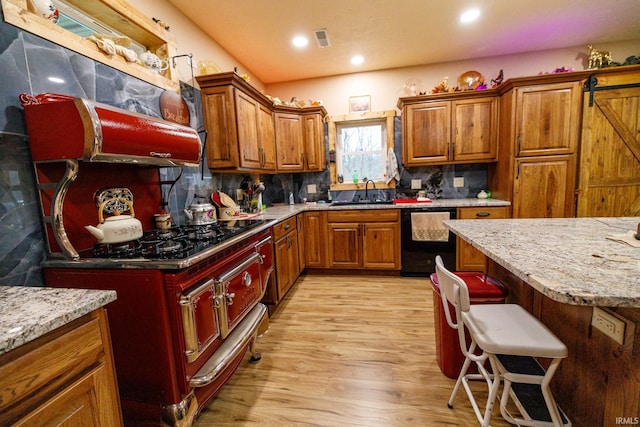 kitchen featuring tasteful backsplash, light stone counters, light hardwood / wood-style flooring, a breakfast bar, and black appliances