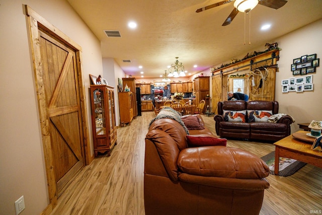 living room featuring ceiling fan with notable chandelier, light hardwood / wood-style floors, and a barn door