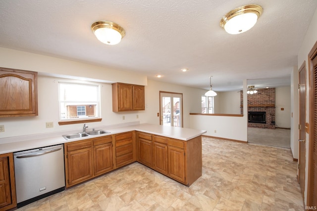 kitchen featuring kitchen peninsula, a brick fireplace, stainless steel dishwasher, sink, and pendant lighting