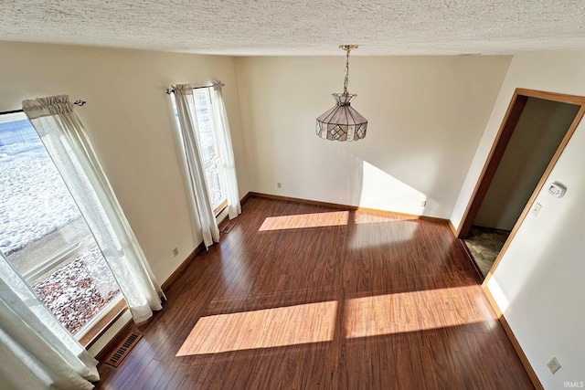 unfurnished dining area with a textured ceiling and dark wood-type flooring