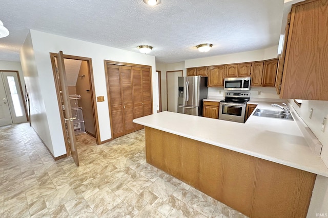 kitchen with kitchen peninsula, appliances with stainless steel finishes, a textured ceiling, and sink