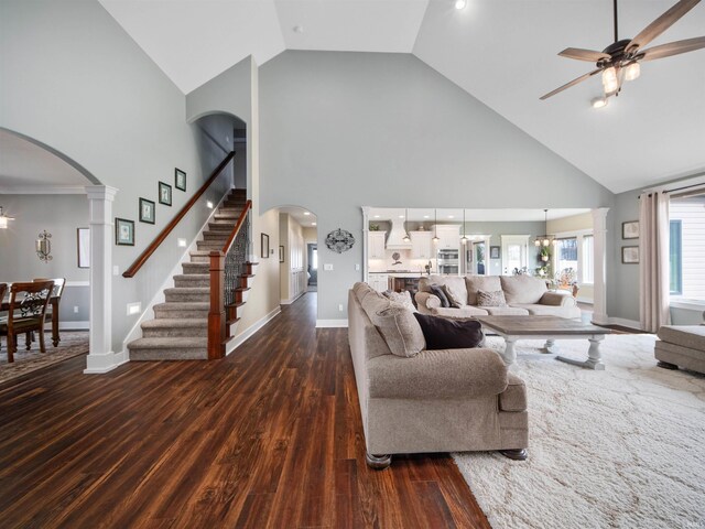 living room featuring ornate columns, high vaulted ceiling, dark wood-type flooring, and ceiling fan with notable chandelier