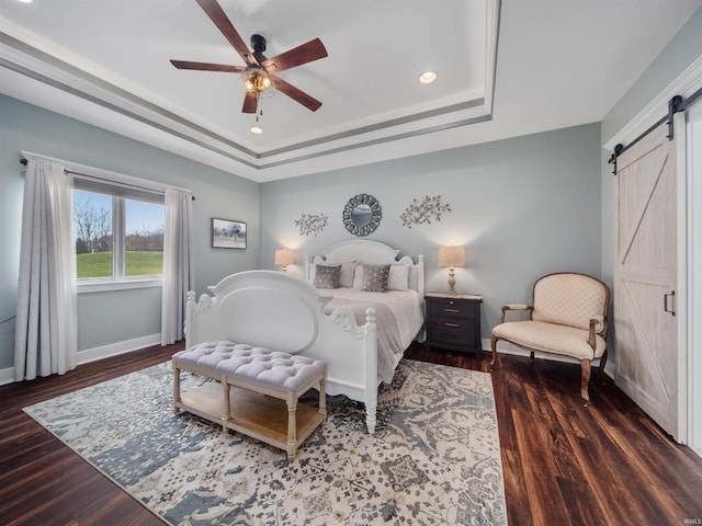 bedroom with a tray ceiling, a barn door, ceiling fan, and dark hardwood / wood-style flooring