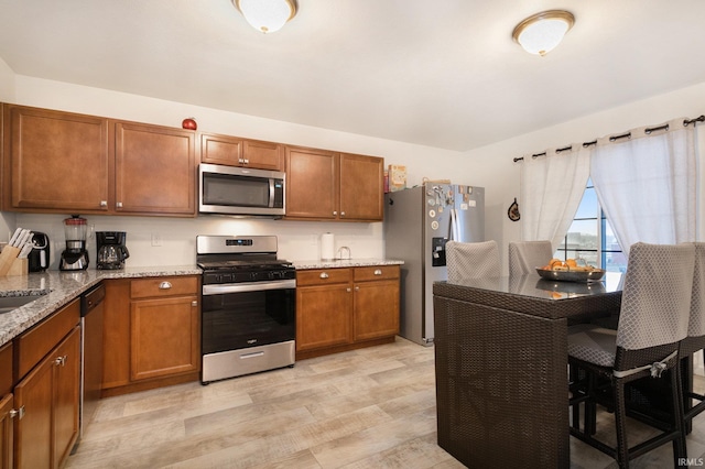 kitchen with sink, stainless steel appliances, light hardwood / wood-style flooring, and light stone counters