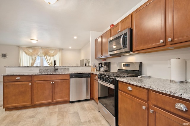 kitchen featuring sink, stainless steel appliances, light stone counters, kitchen peninsula, and light wood-type flooring