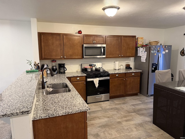 kitchen with sink, light stone countertops, light hardwood / wood-style floors, kitchen peninsula, and stainless steel appliances