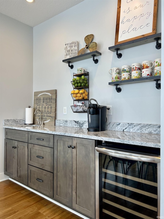 bar with light stone countertops, a textured ceiling, dark hardwood / wood-style flooring, and wine cooler