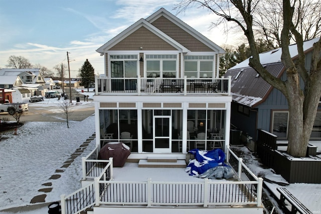 snow covered rear of property featuring a sunroom