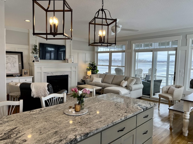 kitchen with light stone countertops, crown molding, decorative light fixtures, a premium fireplace, and light hardwood / wood-style floors