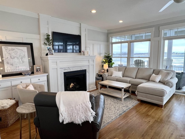 living room with ceiling fan, wood-type flooring, ornamental molding, and a high end fireplace