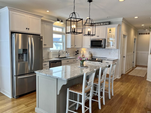 kitchen featuring light stone counters, stainless steel appliances, sink, a center island, and white cabinetry