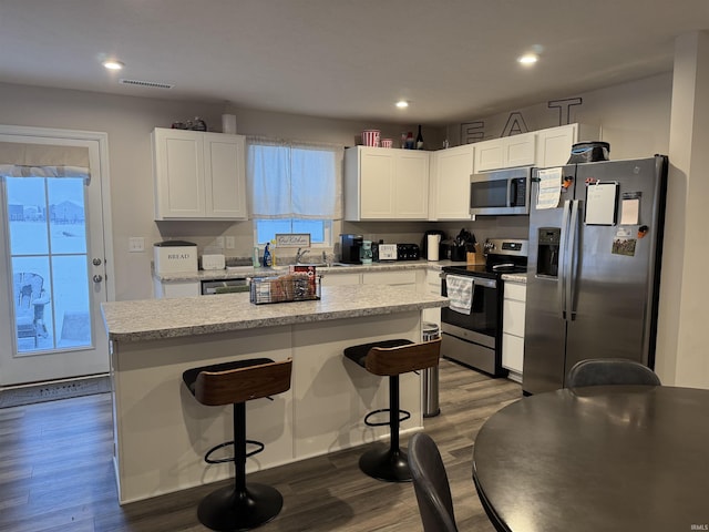 kitchen featuring a center island, a kitchen breakfast bar, dark hardwood / wood-style floors, white cabinetry, and stainless steel appliances