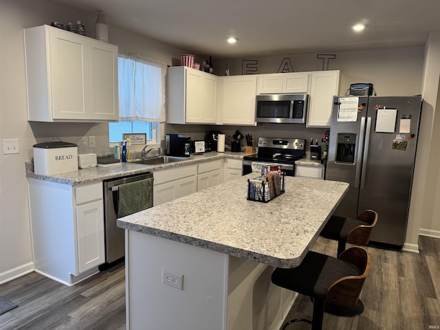 kitchen with dark wood-type flooring, sink, appliances with stainless steel finishes, a kitchen island, and white cabinetry