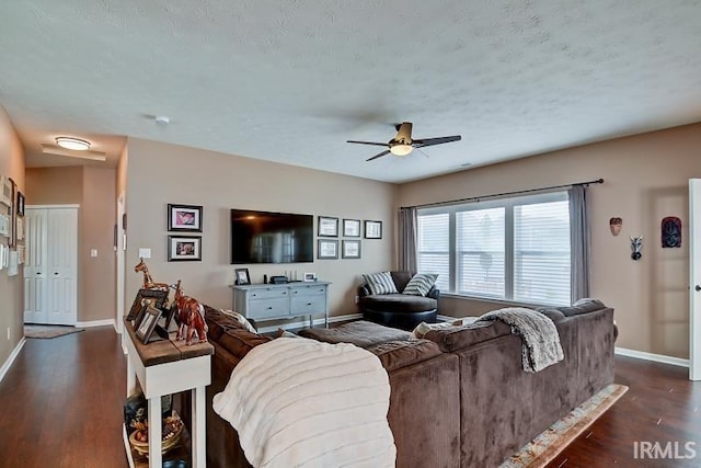 living room with a textured ceiling, ceiling fan, and dark wood-type flooring