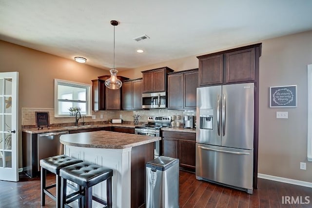 kitchen featuring dark wood-type flooring, sink, appliances with stainless steel finishes, decorative light fixtures, and a kitchen island