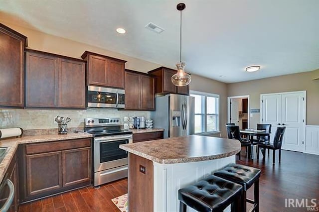 kitchen featuring hanging light fixtures, dark hardwood / wood-style floors, dark brown cabinets, a kitchen island, and appliances with stainless steel finishes