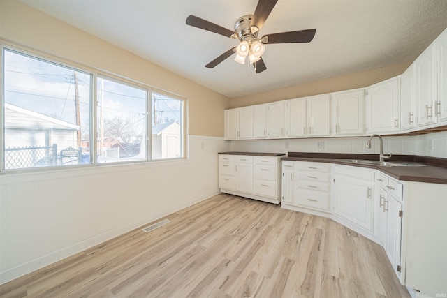 kitchen with ceiling fan, white cabinetry, sink, and light hardwood / wood-style flooring