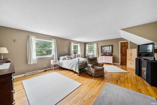 bedroom featuring vaulted ceiling, wood-type flooring, and a textured ceiling