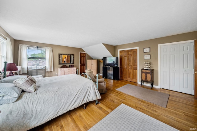 bedroom with wood-type flooring, lofted ceiling, and multiple closets