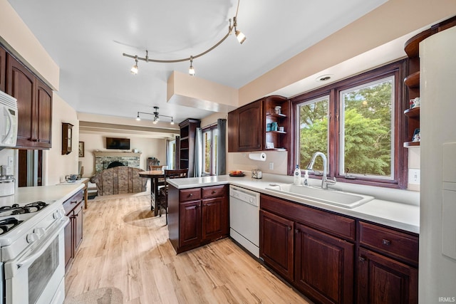 kitchen with sink, a stone fireplace, light hardwood / wood-style flooring, kitchen peninsula, and white appliances