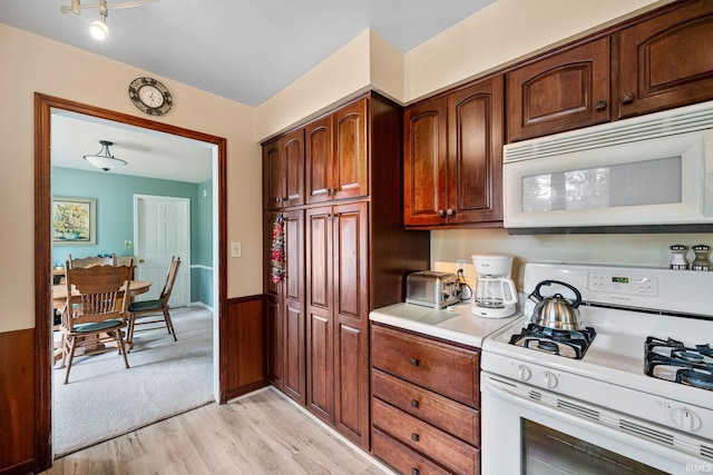 kitchen with light wood-type flooring, white appliances, and wooden walls