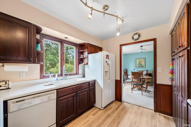 kitchen with dark brown cabinetry, sink, light hardwood / wood-style flooring, white appliances, and wooden walls