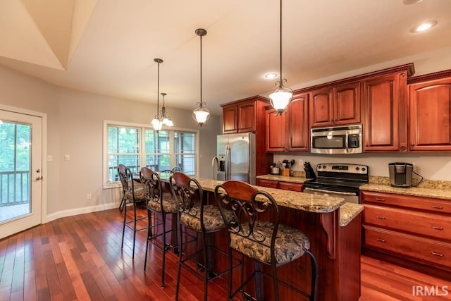 kitchen with a kitchen bar, appliances with stainless steel finishes, a center island with sink, and hanging light fixtures