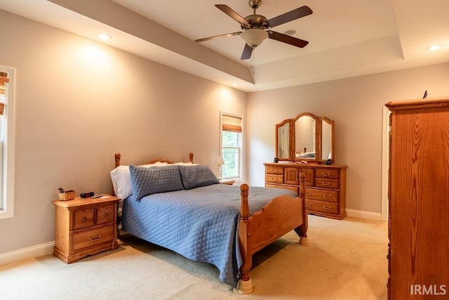 carpeted bedroom with a raised ceiling and ceiling fan