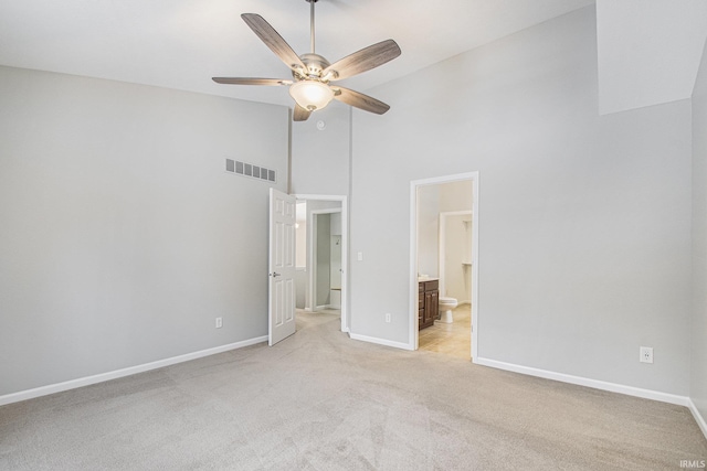 unfurnished bedroom featuring light carpet, connected bathroom, high vaulted ceiling, and ceiling fan