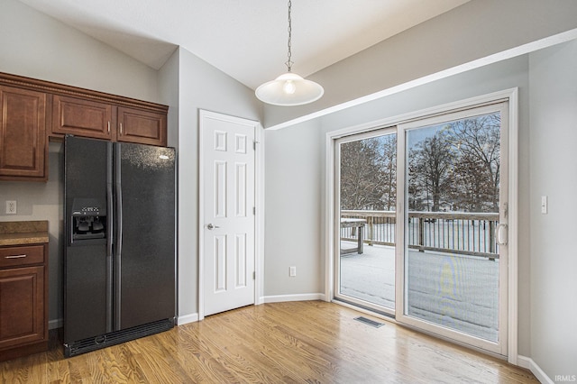 kitchen with black fridge with ice dispenser, light hardwood / wood-style flooring, hanging light fixtures, and lofted ceiling