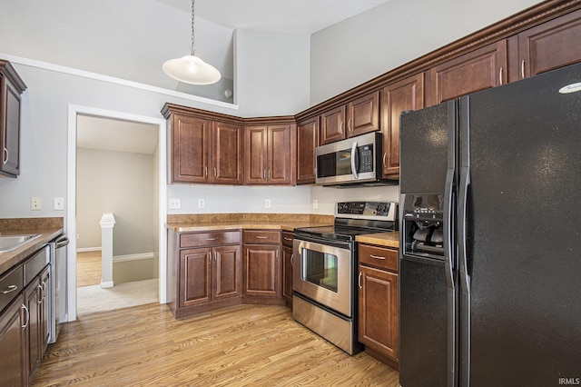 kitchen featuring sink, a towering ceiling, decorative light fixtures, appliances with stainless steel finishes, and light wood-type flooring