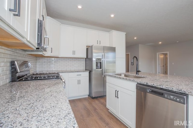 kitchen featuring tasteful backsplash, light stone counters, stainless steel appliances, sink, and white cabinetry