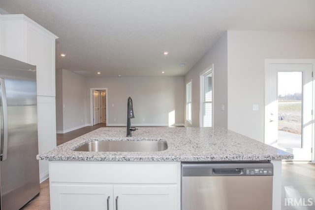 kitchen featuring light stone countertops, appliances with stainless steel finishes, sink, a center island with sink, and white cabinets