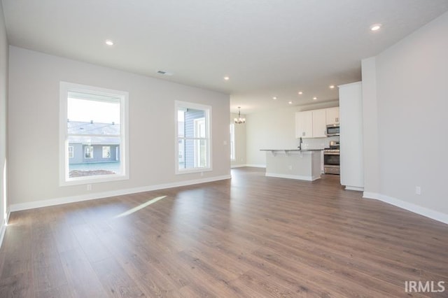 unfurnished living room featuring dark hardwood / wood-style flooring, sink, and an inviting chandelier