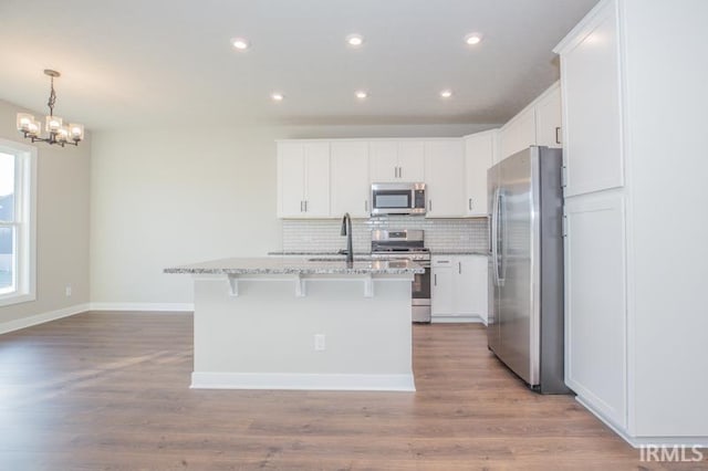 kitchen featuring white cabinetry, light stone countertops, stainless steel appliances, light hardwood / wood-style flooring, and a kitchen island with sink