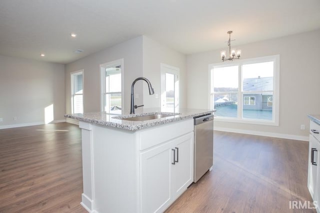 kitchen featuring stainless steel dishwasher, sink, decorative light fixtures, white cabinets, and an island with sink