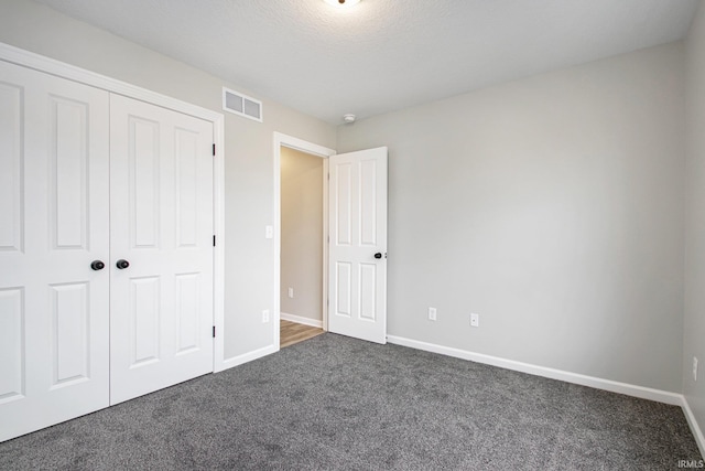 unfurnished bedroom featuring dark carpet, a textured ceiling, and a closet