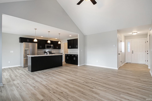 kitchen featuring appliances with stainless steel finishes, decorative light fixtures, a kitchen island with sink, and light hardwood / wood-style floors