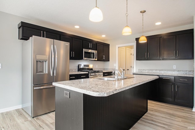 kitchen with sink, stainless steel appliances, light hardwood / wood-style flooring, an island with sink, and decorative light fixtures