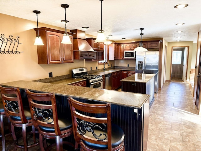 kitchen featuring kitchen peninsula, premium range hood, stainless steel appliances, sink, and decorative light fixtures