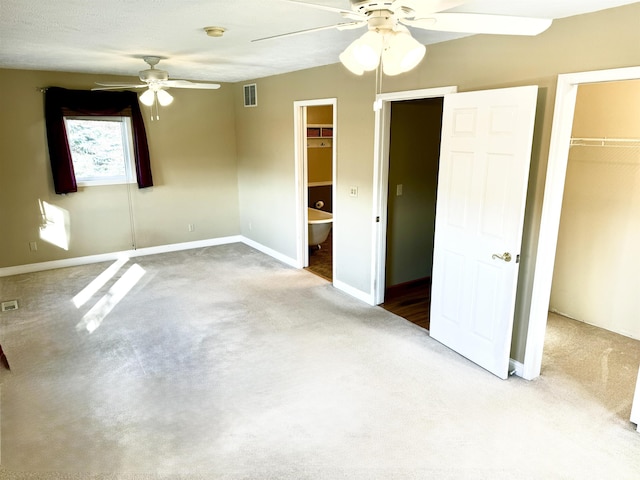 unfurnished bedroom with a walk in closet, ceiling fan, a closet, and ensuite bath