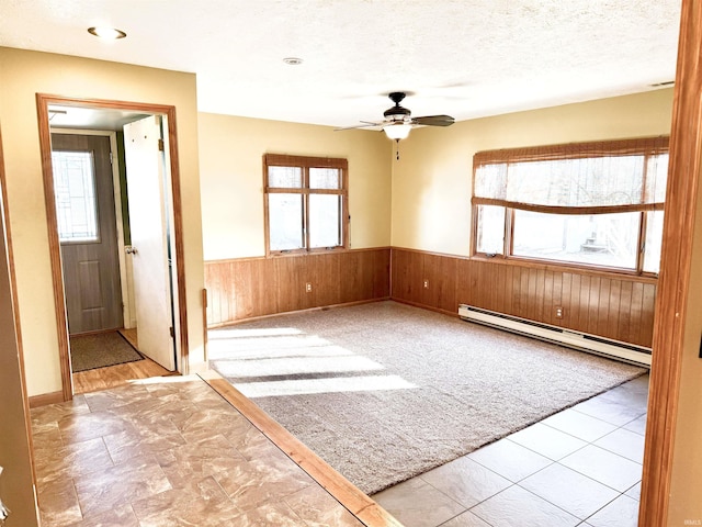 unfurnished room with a textured ceiling, ceiling fan, wood walls, and a baseboard heating unit