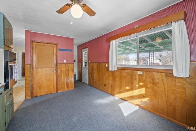 interior space with carpet floors, wood walls, and ceiling fan