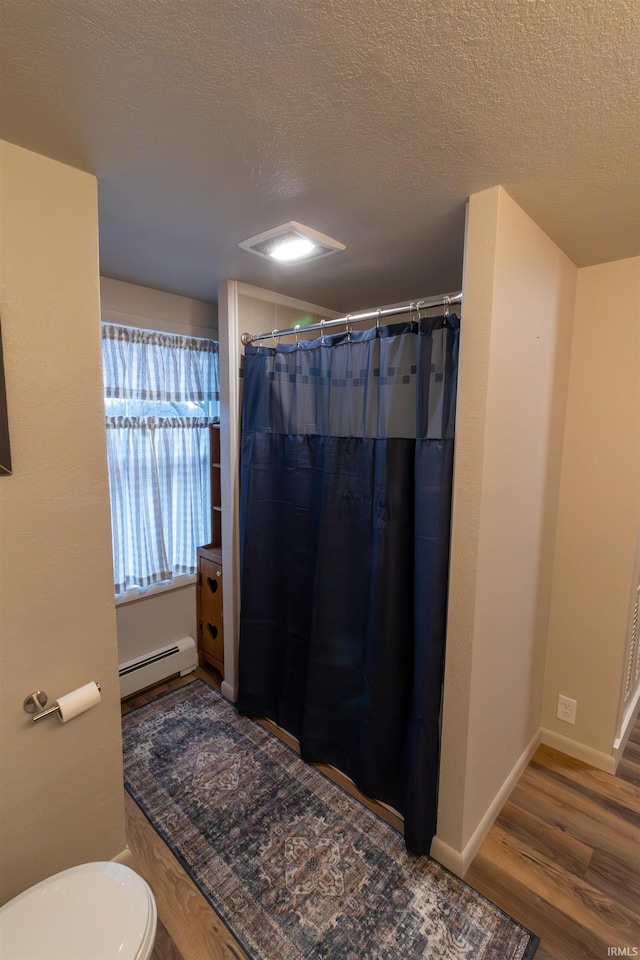 bathroom with a textured ceiling, toilet, wood-type flooring, and baseboard heating